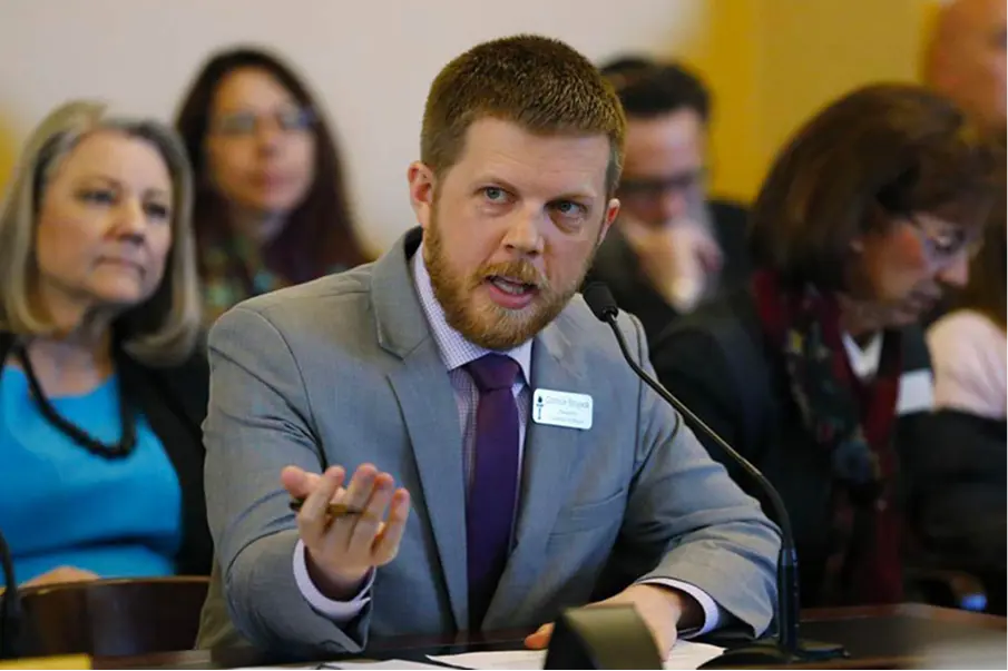Man in a suit speaking during a meeting while attendees listen.