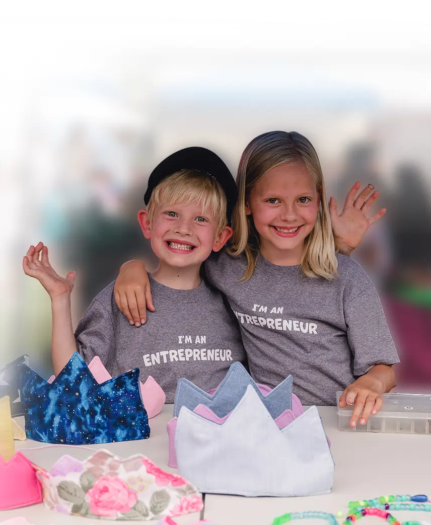 Two smiling children wearing entrepreneur shirts behind colorful handmade crowns.